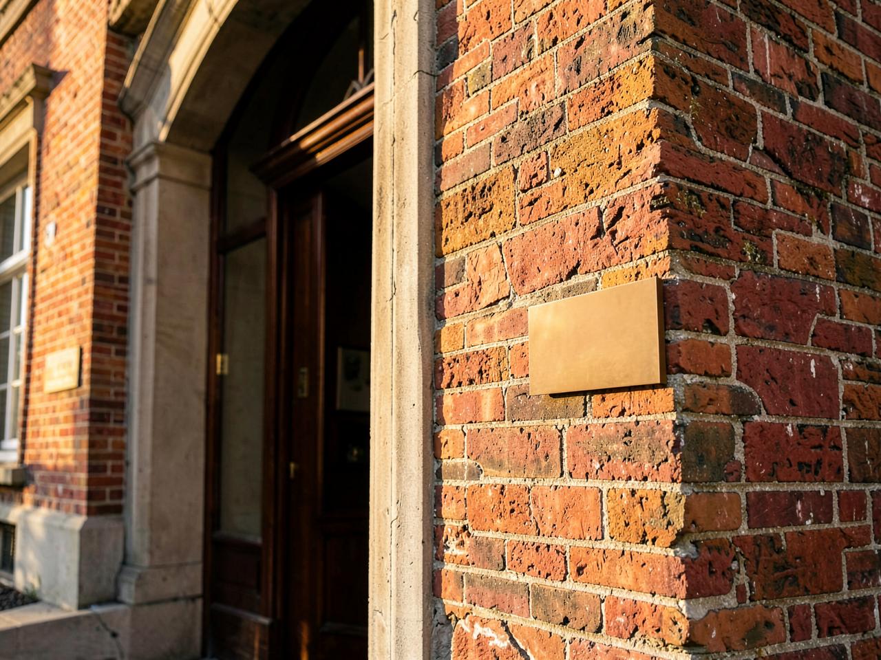 The arched brick entrance of a historic building with a small brass plaque mounted beside the doorway